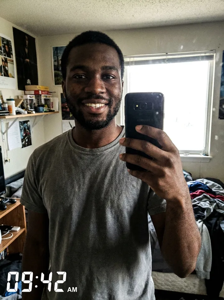 Casual bedroom selfie of a young man in a t-shirt with a cluttered background