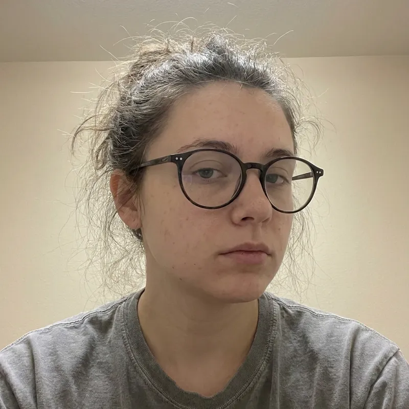 AI demo face before glow-up: a makeup-free woman with glasses, frizzy hair and dull skin in flat light